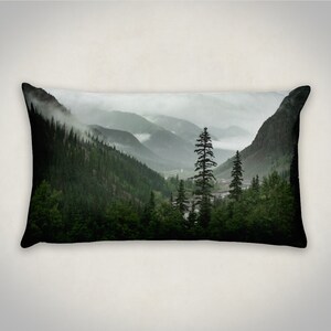 May include: A scenic pillow featuring a misty mountain landscape with a tall evergreen tree in the foreground. The mountains are covered in lush green trees and fog.