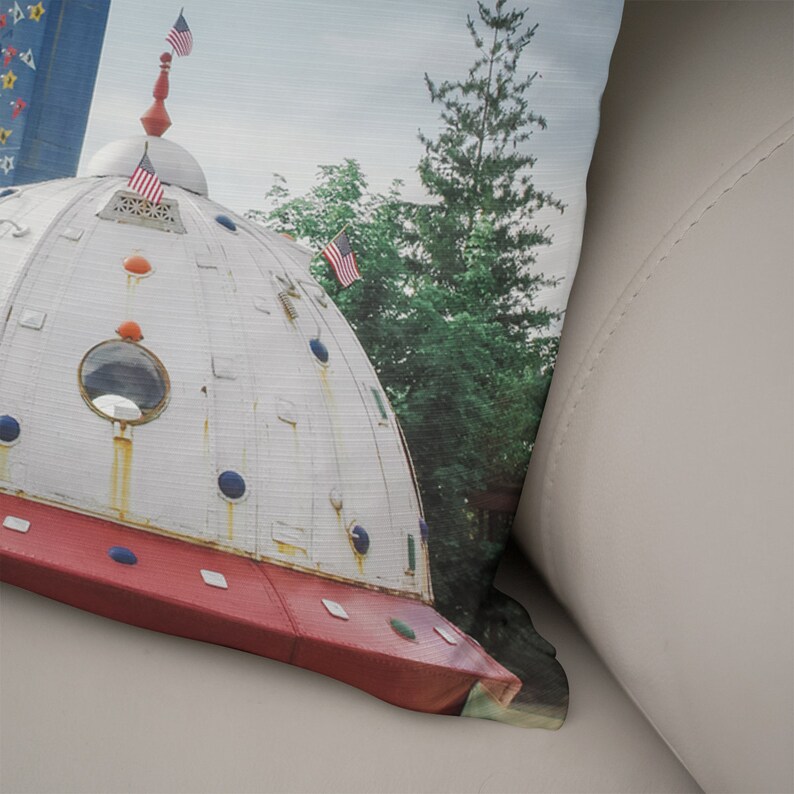 May include: A white and red dome-shaped structure with a round window and blue and red accents. The structure is topped with a spire and two American flags. The structure is surrounded by green trees.