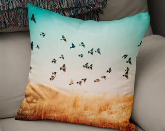 Puede incluir: Una almohada con un fondo degradado azul y blanco que presenta una bandada de pájaros volando en formación contra un atardecer dorado.