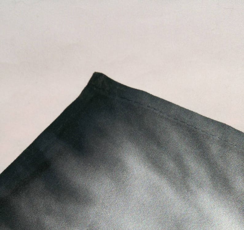 May include: Close-up of a black fabric with a smooth, slightly shiny texture. The fabric is folded over on itself, creating a sharp crease.