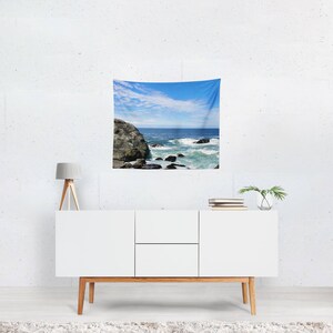 May include: A tapestry featuring a scenic ocean view with crashing waves and a rocky shoreline. The sky is a bright blue with white clouds.