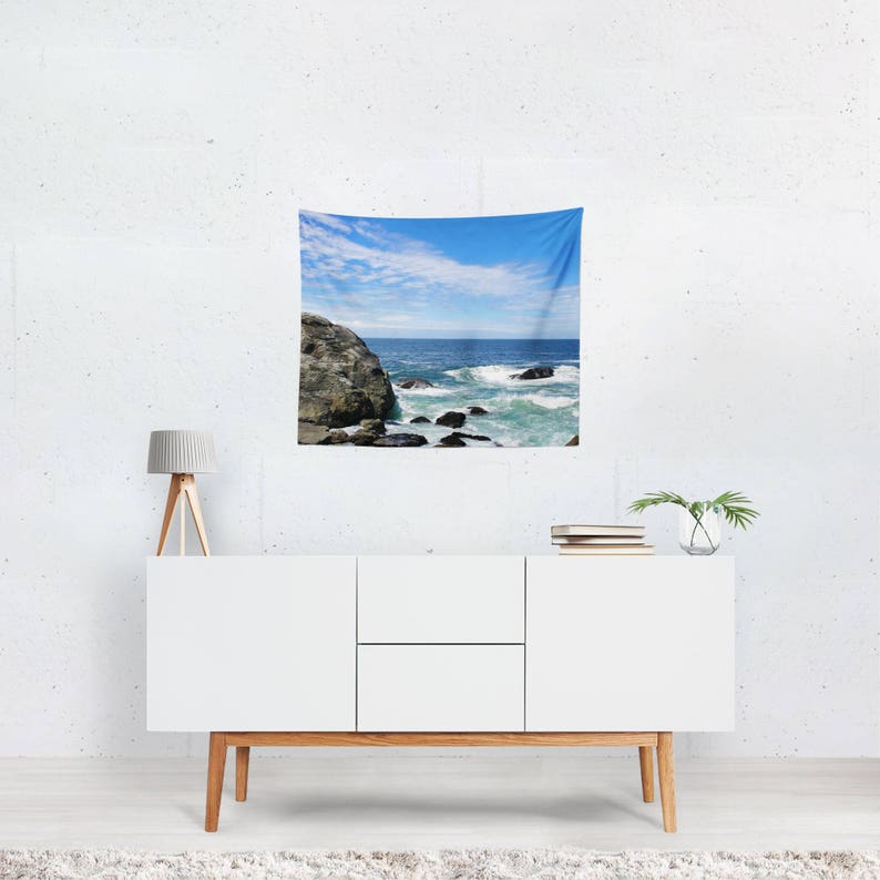 May include: A tapestry featuring a scenic ocean view with crashing waves and a rocky shoreline. The sky is a bright blue with white clouds.