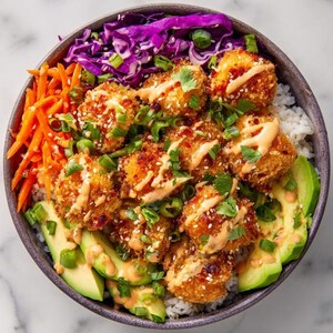 Può includere: Una ciotola colorata di cibo con elementi fritti croccanti e dorati, conditi con una salsa cremosa, cosparsi di semi di sesamo e guarniti con cipollotti e coriandolo. La ciotola contiene anche riso bianco, avocado a fette, carote grattugiate e cavolo rosso.