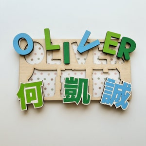 May include: A wooden puzzle board with the name "Oliver" spelled out in blue and green letters. The board has a polka dot pattern and the letters are placed in individual slots. The word "Oliver" is also written in Chinese characters below the letters.