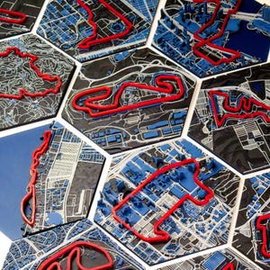 May include: A collection of hexagonal tiles featuring detailed maps with red, raised track outlines. The maps are primarily black and white, with blue accents representing buildings and structures. The tiles are arranged to showcase various race circuits.