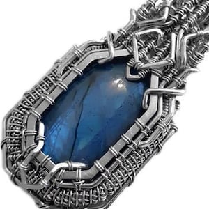 Peut inclure: Pendentif artisanal avec une pierre précieuse bleue sertie dans un fil d'argent. Le fil est tissé autour de la pierre, créant un design unique et artistique. La pierre a une surface polie et une couleur bleu profond.