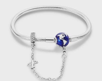 May include: A silver bracelet with a snake chain design. The bracelet features a charm with a blue globe design and a small airplane charm. The globe charm has white continents on a blue background. The airplane charm is connected to the bracelet with a chain.