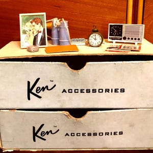 May include: A vintage-style dollhouse display featuring miniature accessories. Includes a framed picture, a small alarm clock, a radio, and other tiny items. The box below is labeled "Ken ACCESSORIES".