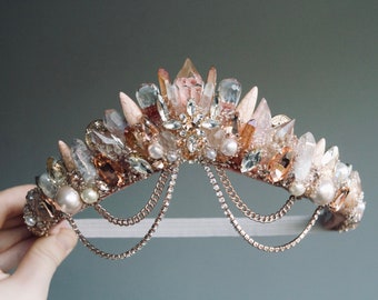 May include: A delicate crown made of crystals and pearls, with a gold chain detail. The crown is designed in a whimsical style, with a variety of shapes and sizes of crystals.
