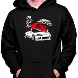 May include: Black hoodie with a white car graphic, a red sun, and Japanese text. The car is a white sports car with a detailed front end. The design is a stylized illustration.
