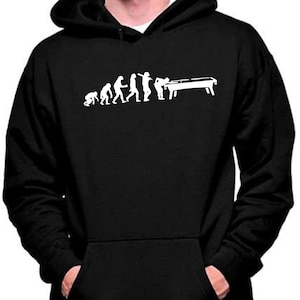 Puede incluir: Sudadera con capucha negra con un gráfico blanco que representa la evolución del hombre, culminando con una persona jugando al billar. El diseño muestra una progresión de figuras simiescas a una persona con un taco de billar.