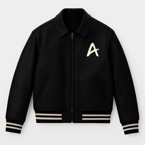 May include: Black bomber jacket with a white "A" on the chest. The jacket has a collar, a zip closure, and two front pockets. The cuffs and hem feature cream-coloured stripes.