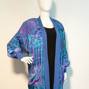 May include: A long, blue, patchwork cardigan with a floral and geometric print. The cardigan has a shawl collar and long sleeves.