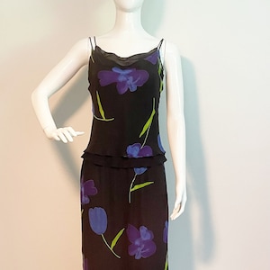 以下が含まれることがあります： 青い花と緑の花が描かれた花柄の黒いスリップドレス。ドレスは体にフィットしたボディとゆったりとしたスカートになっています。