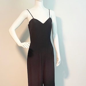 May include: A black sleeveless jumpsuit with a V-neckline. The jumpsuit has a wide leg and is made of a smooth fabric.