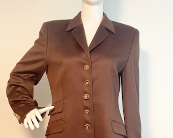 May include: A brown blazer with a notched collar and gold buttons. The blazer has two flap pockets on the front and a single button cuff on each sleeve.