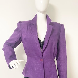 May include: A purple blazer with a single button closure and a fitted silhouette. The blazer has a textured fabric and a slightly puffed shoulder.