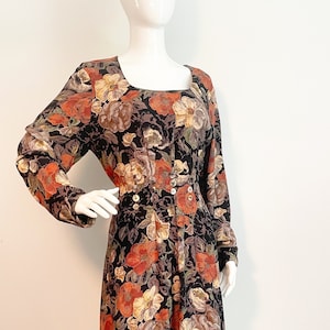 May include: A black floral dress with long sleeves and a square neckline. The dress has a fitted bodice and a flowing skirt. The floral pattern is in shades of orange, brown, and cream.