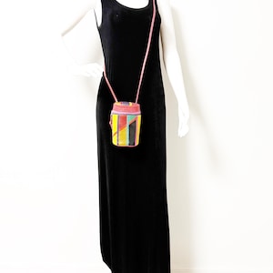 May include: A black velvet maxi dress with a small, colorful, geometric-patterned crossbody bag. The bag features pink, yellow, green, and black sections. The bag has a pink strap.