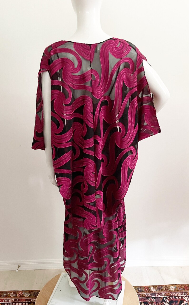 May include: A long, black and magenta dress with a flowing, abstract pattern. The dress is made of a sheer fabric with a delicate, embroidered design.