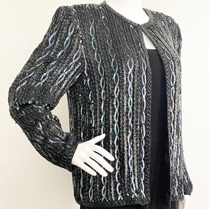 May include: A black sequined jacket with a long-sleeved design. The sequins are iridescent and create a shimmering effect.