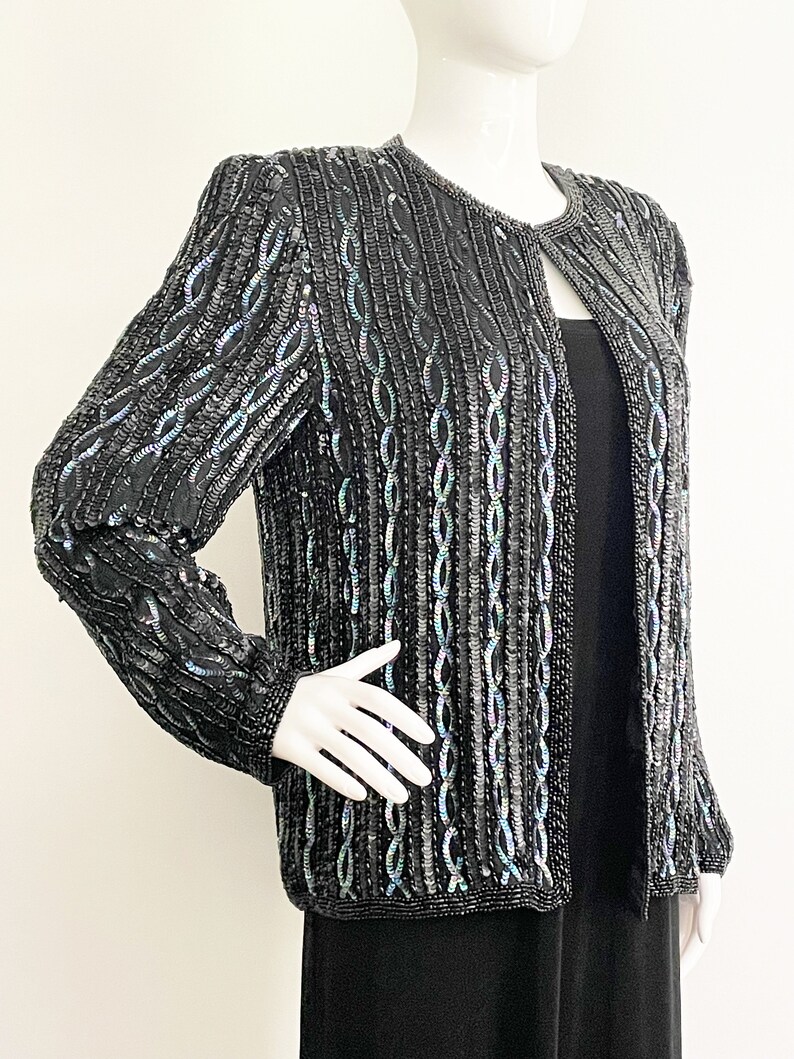 May include: A black sequined jacket with a long-sleeved design. The sequins are iridescent and create a shimmering effect.