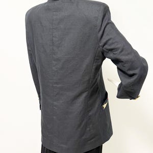 Puede incluir: Un blazer gris oscuro con cuello cl&aacute;sico y mangas largas. El blazer presenta detalles dorados en forma de estrella en los bolsillos y pu&ntilde;os. La prenda se exhibe en un maniqu&iacute;.