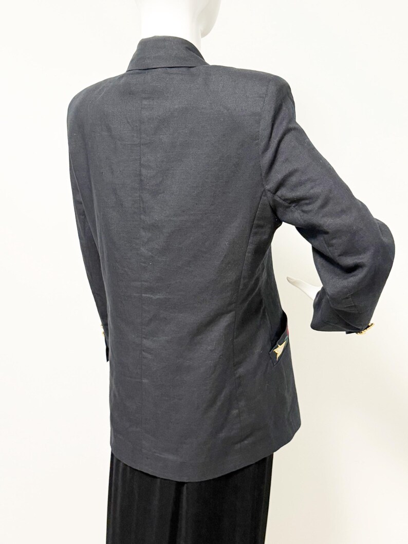 Puede incluir: Un blazer gris oscuro con cuello cl&aacute;sico y mangas largas. El blazer presenta detalles dorados en forma de estrella en los bolsillos y pu&ntilde;os. La prenda se exhibe en un maniqu&iacute;.