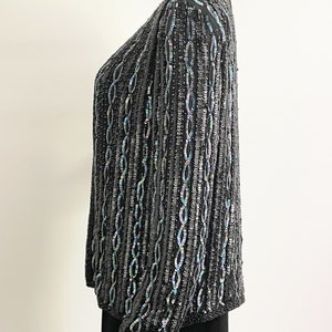 May include: A black sequined cardigan with iridescent sequins. The cardigan has a V-neck and long sleeves.