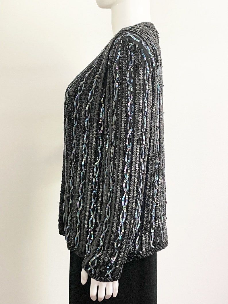 May include: A black sequined cardigan with iridescent sequins. The cardigan has a V-neck and long sleeves.