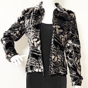 May include: Black velvet jacket with a botanical pattern in shades of beige and gray. The jacket has a high collar, long sleeves, and a full-length zipper. The jacket is displayed on a mannequin.