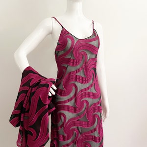 May include: A long, pink, sheer dress with a black swirl pattern. The dress has thin straps and a loose fit.