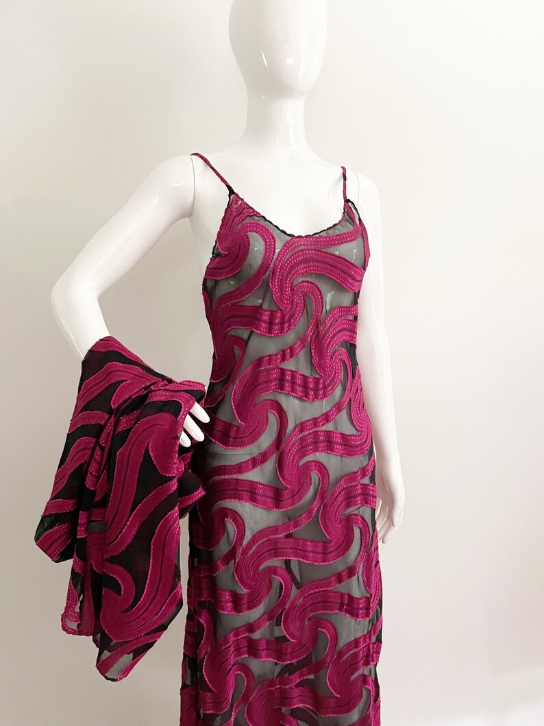 May include: A long, pink, sheer dress with a black swirl pattern. The dress has thin straps and a loose fit.
