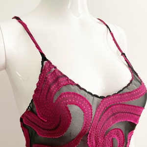 May include: A black sheer slip dress with a pink floral pattern. The floral pattern is made of a textured fabric and is layered over the sheer fabric.