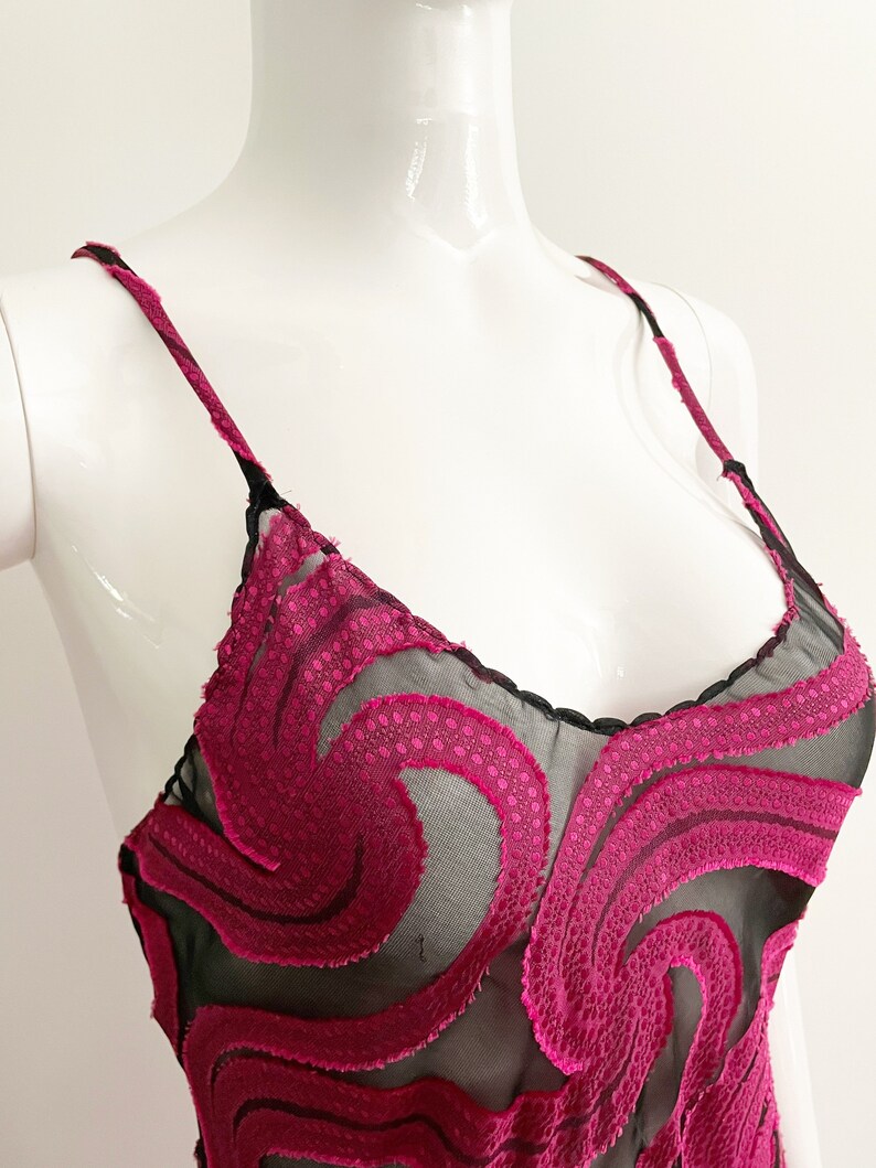 May include: A black sheer slip dress with a pink floral pattern. The floral pattern is made of a textured fabric and is layered over the sheer fabric.