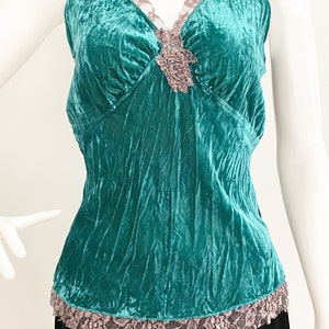 May include: Teal blue velvet sleeveless top with a lace trim and a floral embellishment at the neckline.