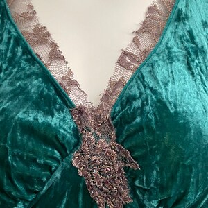 May include: A deep green velvet top with a V-neckline and a delicate lace trim. The lace is embellished with small beads and has a floral design.