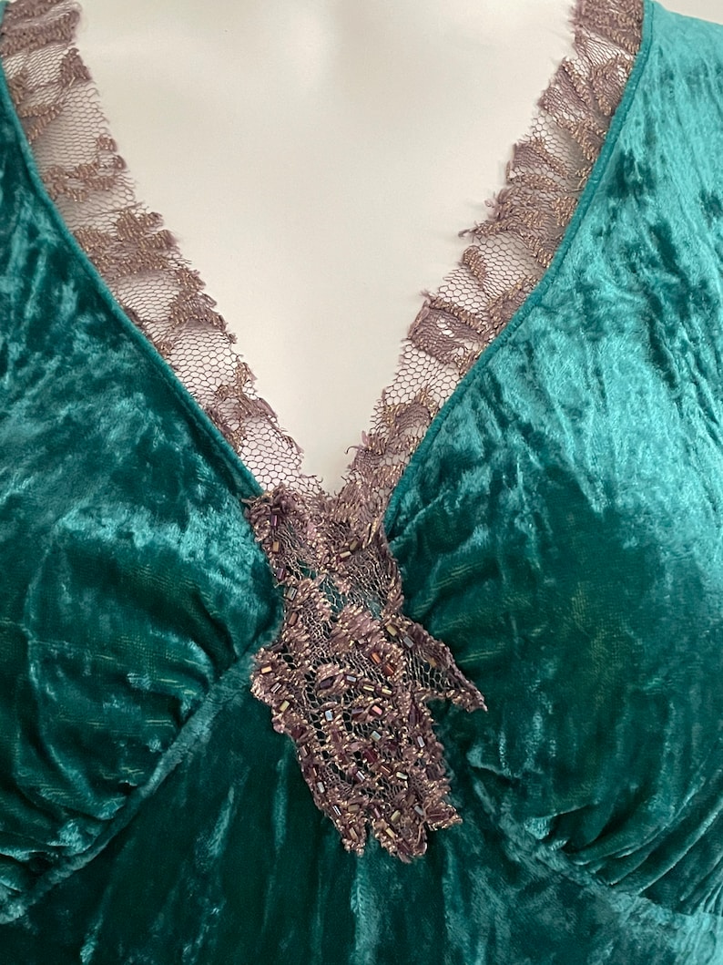 May include: A deep green velvet top with a V-neckline and a delicate lace trim. The lace is embellished with small beads and has a floral design.