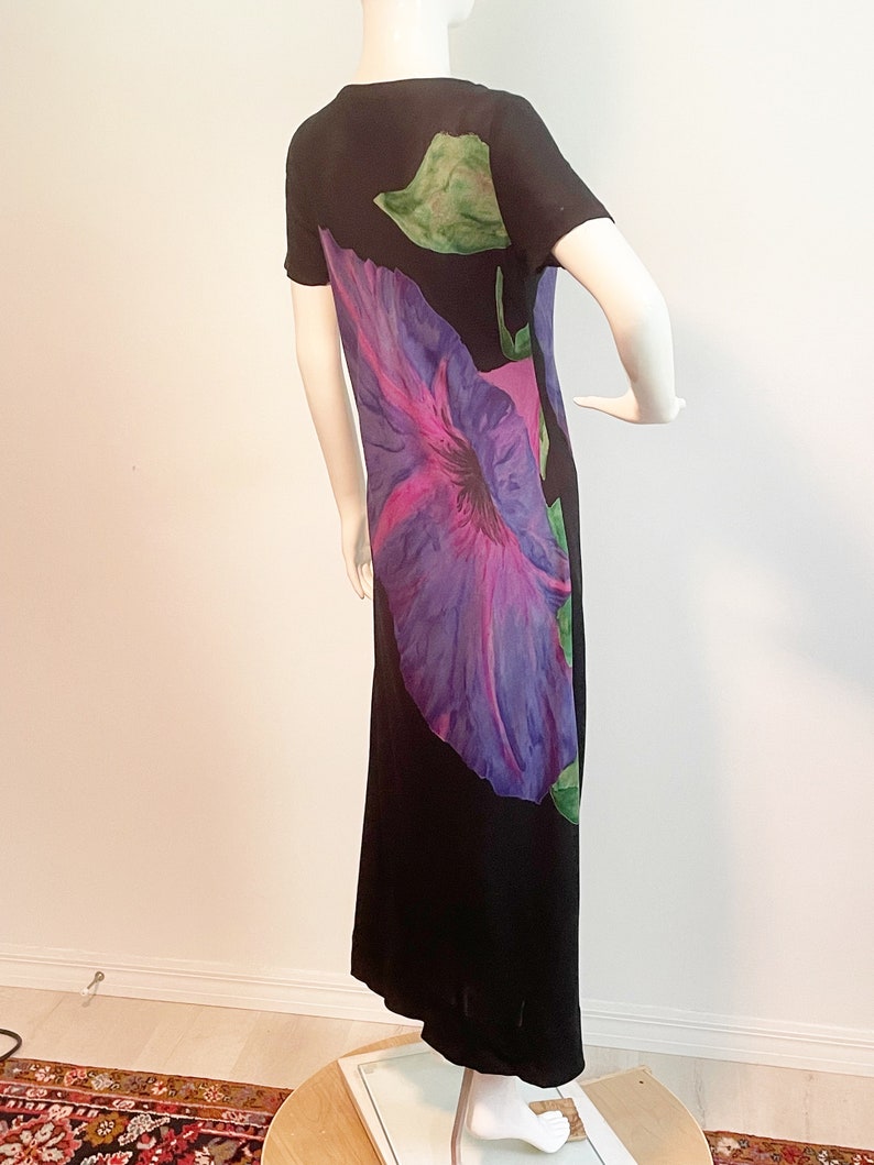 May include: A black maxi dress with a large purple and pink flower print. The dress has short sleeves and a scoop neck.