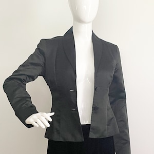 May include: A black satin blazer with a notched collar and a single button fastening. The blazer has a fitted silhouette and long sleeves.