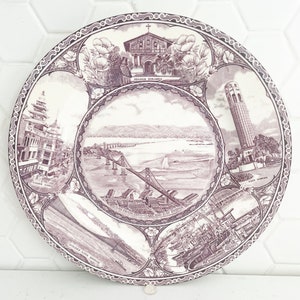 May include: A vintage ceramic plate with a purple design featuring iconic landmarks of San Francisco, including the Golden Gate Bridge, Coit Tower, and Mission Dolores. The plate is decorated with a floral border.