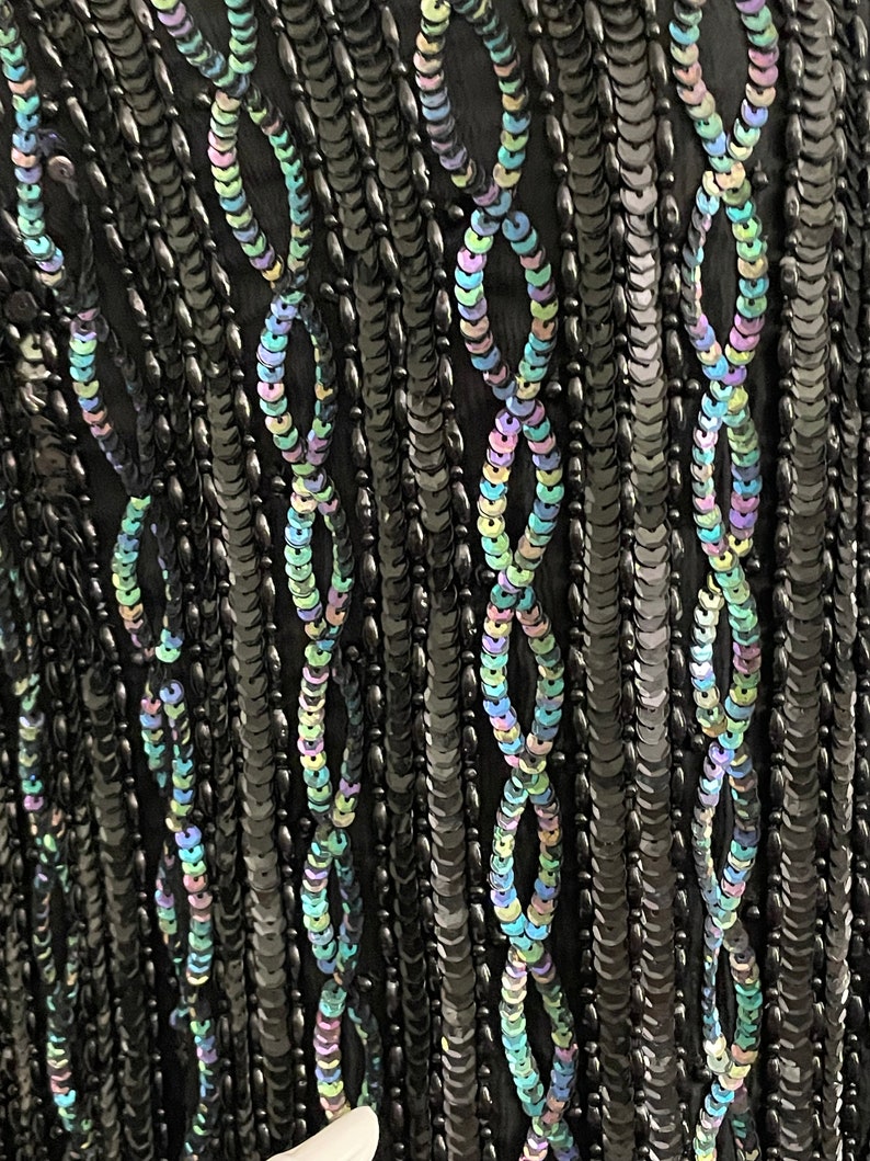 May include: Black fabric with iridescent sequins arranged in a vertical pattern. The sequins are arranged in a repeating pattern of ovals.