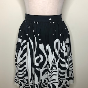 May include: A black and white patterned skirt with a full, gathered silhouette. The skirt has a black waistband and a white trim at the hem.