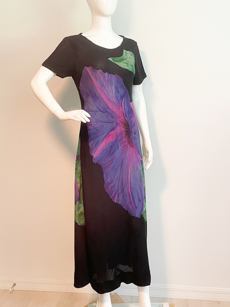 May include: A black maxi dress with a large purple and pink flower print. The dress has short sleeves and a round neckline.