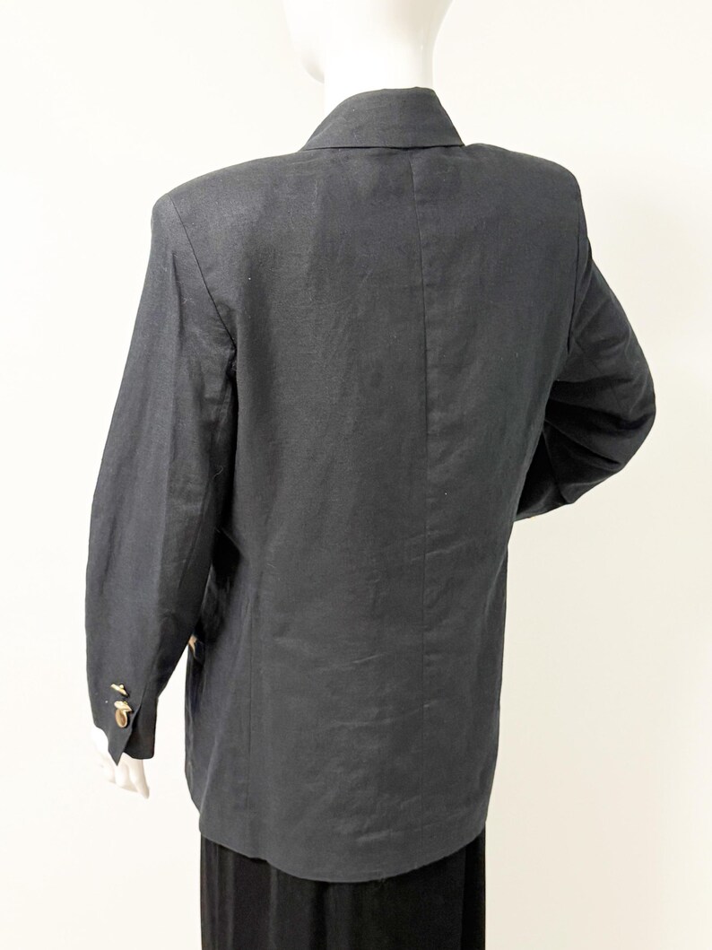 Puede incluir: Un blazer gris oscuro con botones dorados, exhibido en un maniqu&iacute;. El blazer tiene mangas largas y un cuello cl&aacute;sico. La tela parece ser lino o una mezcla de lino. El blazer es de estilo cl&aacute;sico.