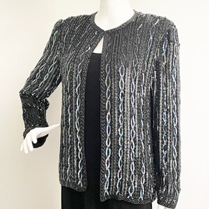 May include: A black sequined jacket with a subtle iridescent sheen. The jacket has a round neckline and long sleeves. The sequins are arranged in a pattern of vertical lines.
