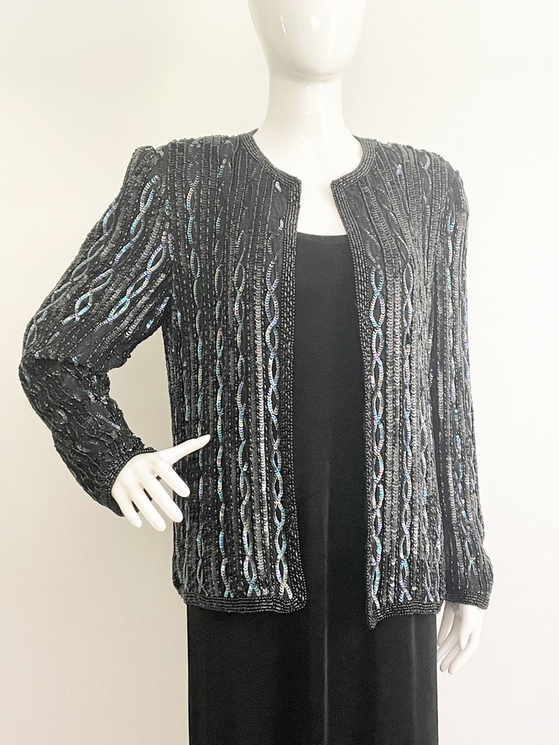 May include: A black beaded jacket with iridescent sequins. The jacket has a round neckline and long sleeves.