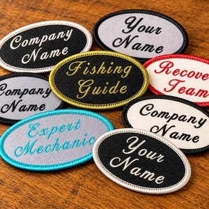 May include: A collection of oval-shaped embroidered patches featuring various text including Company Name, Your Name, Fishing Guide, Recovery Team, and Expert Mechanic. The patches have diverse border colors and thread colors.