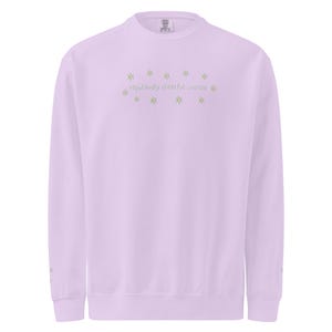 May include: A light purple sweatshirt with the text "repulsively cheerful woman" in a light green color. The text is surrounded by small star-shaped designs. The sweatshirt has long sleeves and a crew neck.