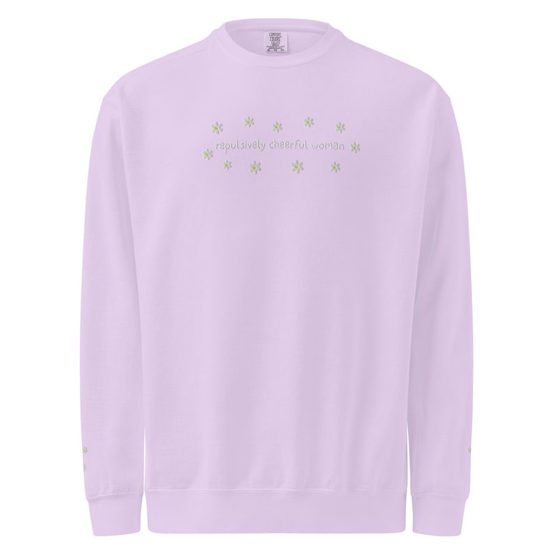 May include: A light purple sweatshirt with the text "repulsively cheerful woman" in a light green color. The text is surrounded by small star-shaped designs. The sweatshirt has long sleeves and a crew neck.
